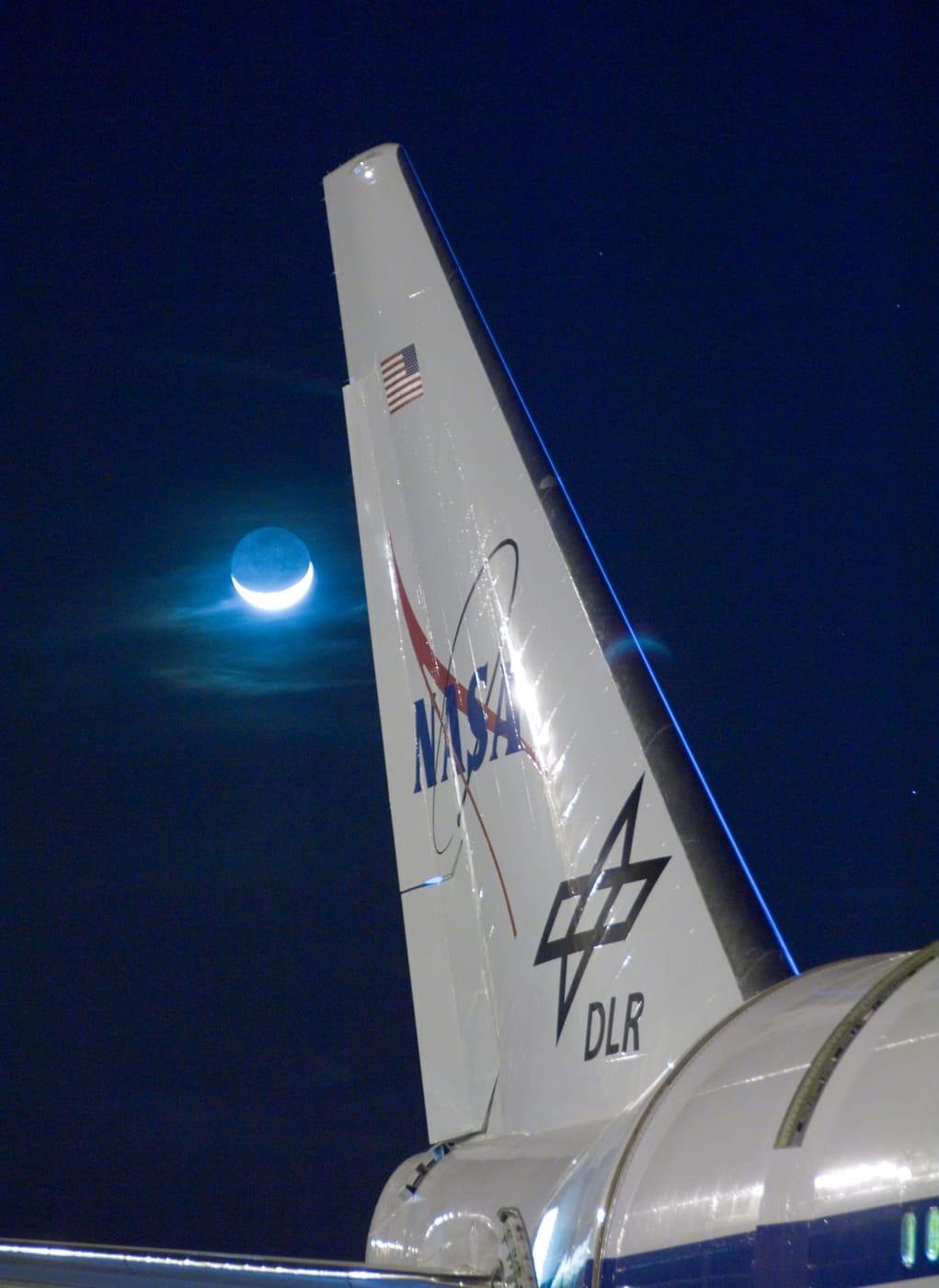 Wispy clouds are illuminated by a bright quarter moon behind the tail of NASA's SOFIA flying observatory during telescope characterization testing in…